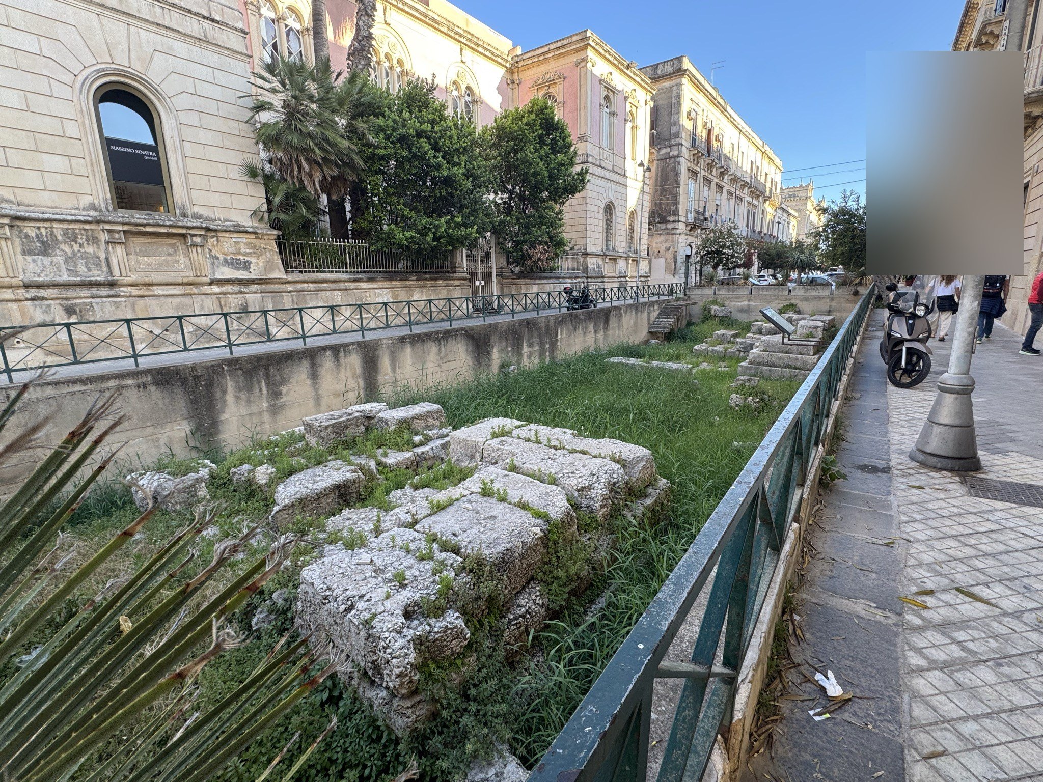 Vista d'insieme dei resti della Porta Urbica di Siracusa lungo via XX Settembre, con palazzi storici e palme sullo sfondo.