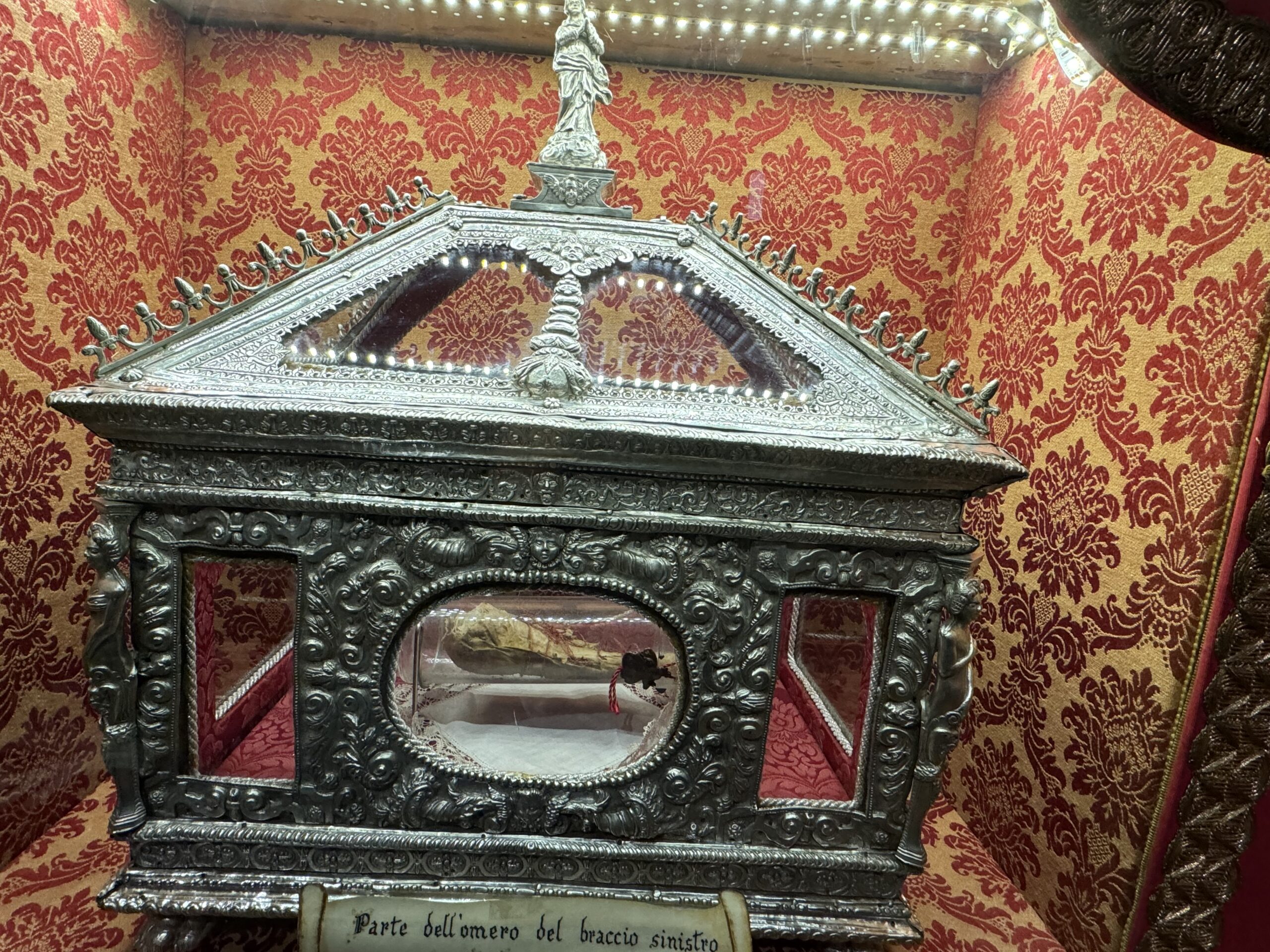 Urna rettangolare in argento e cristallo con coperchio tronco-piramidale e statuetta dell'Immacolata sulla cima: custodisce l'omero del braccio sinistro di santa Lucia donato a Siracusa nel 1988.