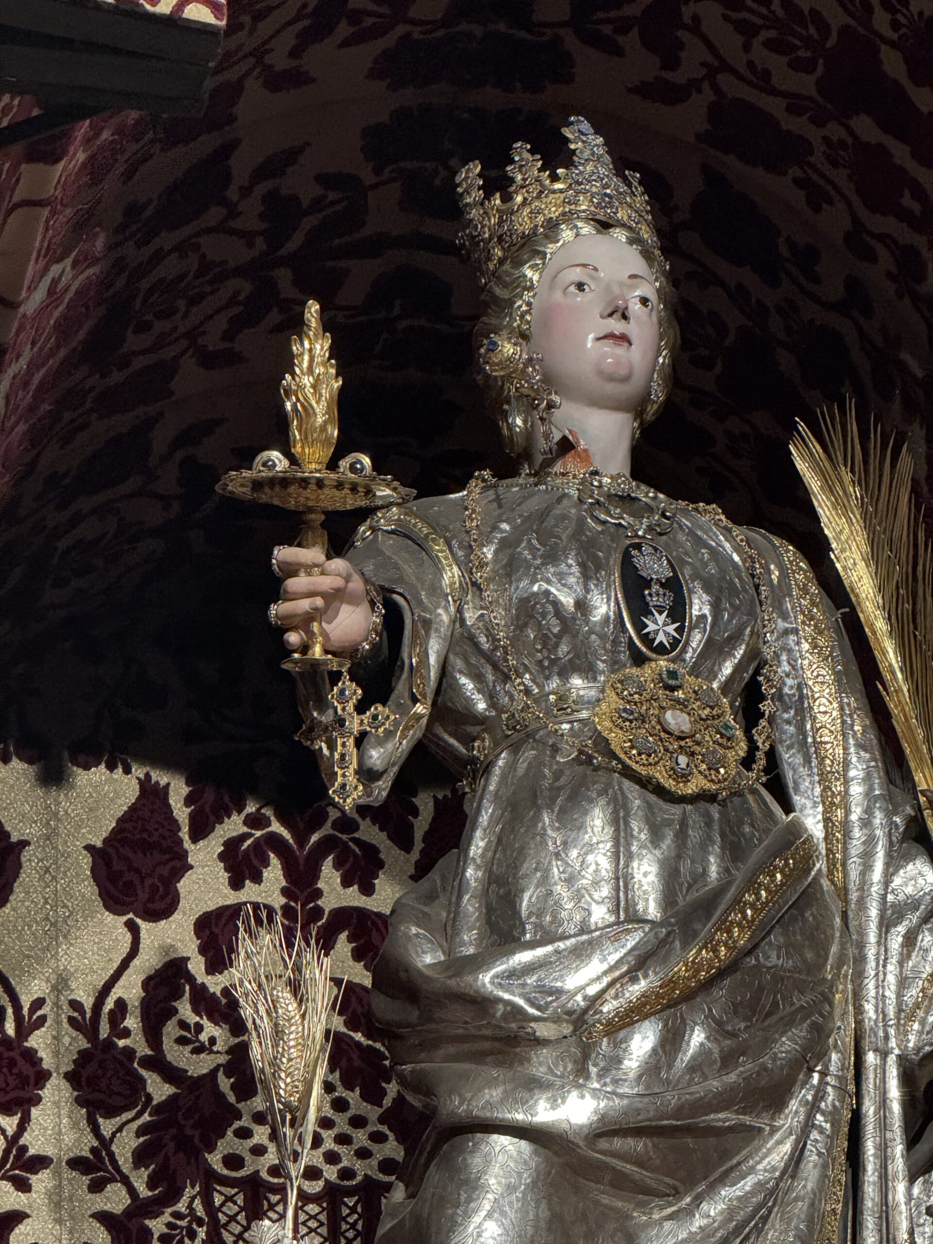 Dettaglio del simulacro argenteo processionale di santa Lucia, con calice, palma del martirio, croce di Malta sul petto, abito cesellato in argento.