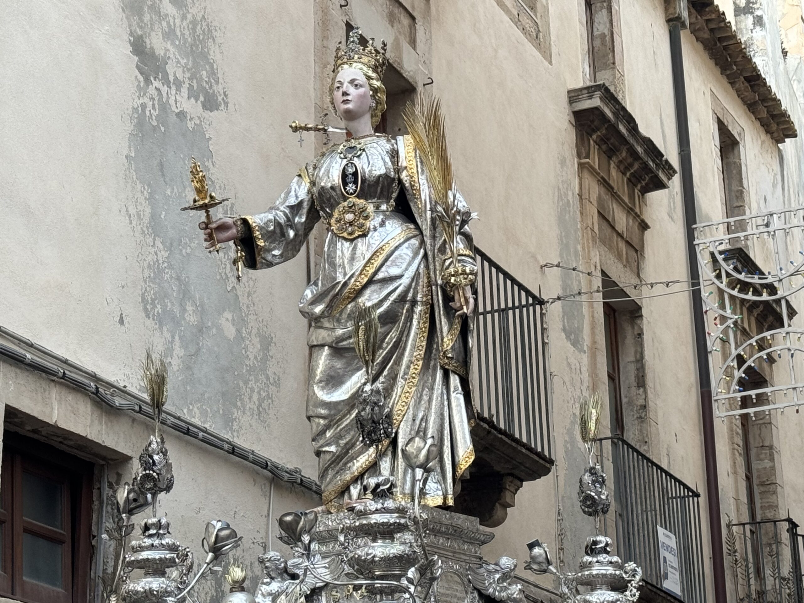 Dettaglio del simulacro argenteo di Santa Lucia durante la processione del 13 dicembre 2023 in una via di Ortigia, con sfondo di muro in pietra calcarea