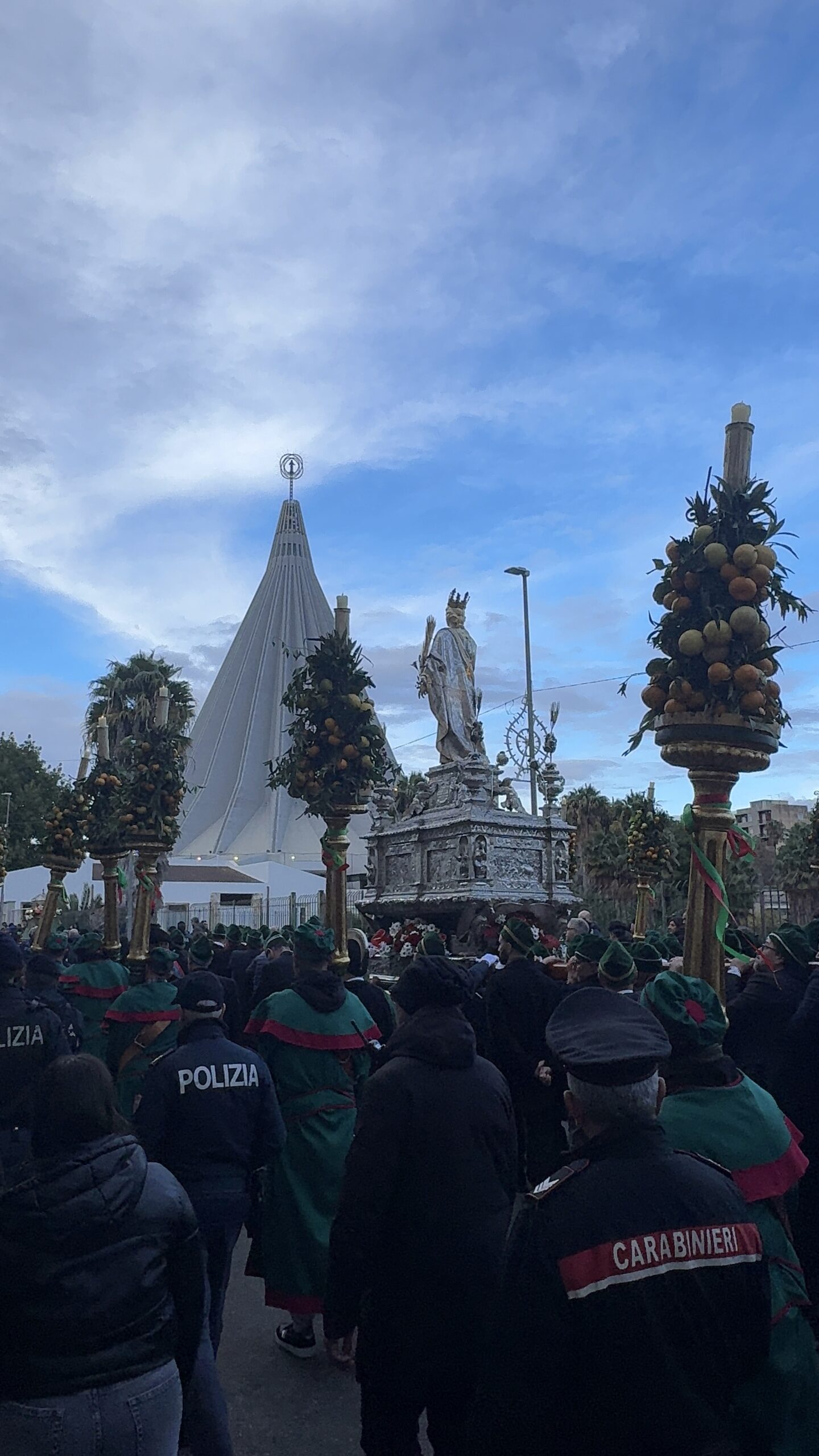 Simulacro argenteo di Santa Lucia con aste decorative cariche di frutti tropicali davanti al cono bianco del Santuario della Madonna delle Lacrime di Siracusa, Polizia di Stato e Carabinieri in primo piano
