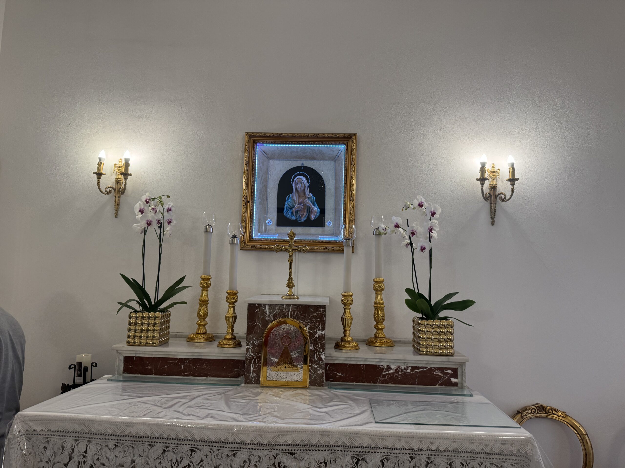 Altare in marmo rosso con tovaglia di pizzo bianco; sopra, il quadretto del Cuore Immacolato in cornice dorata retroilluminata, fra due appliques e due orchidee bianche