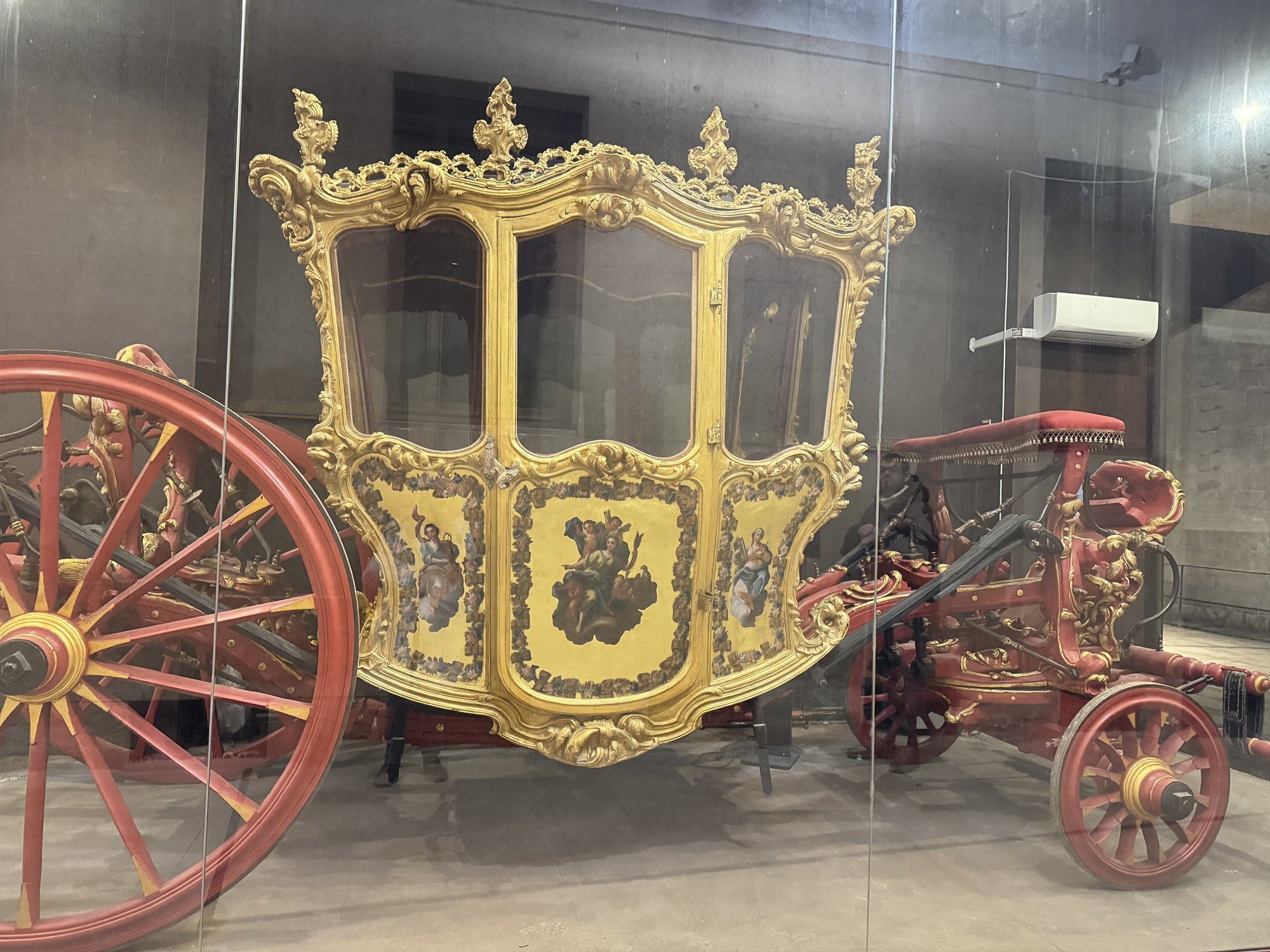 Veduta di tre quarti della carrozza con avantreno e grandi ruote a raggi dipinte di rosso e sospensione a cinghioni di cuoio