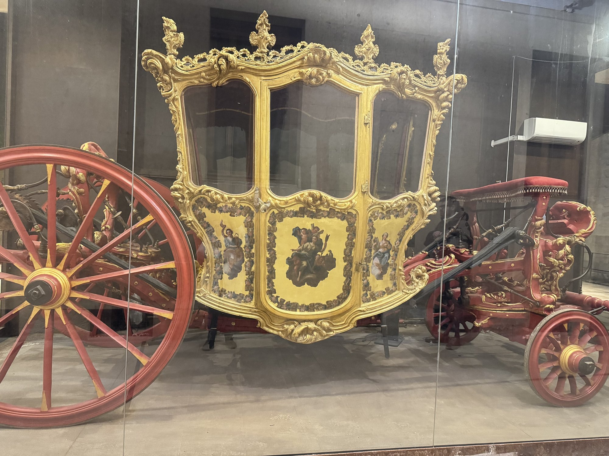 Carrozza cerimoniale settecentesca dorata con cassa intagliata e grandi ruote rosse, entro una teca di vetro nell'androne di Palazzo Vermexio a Siracusa
