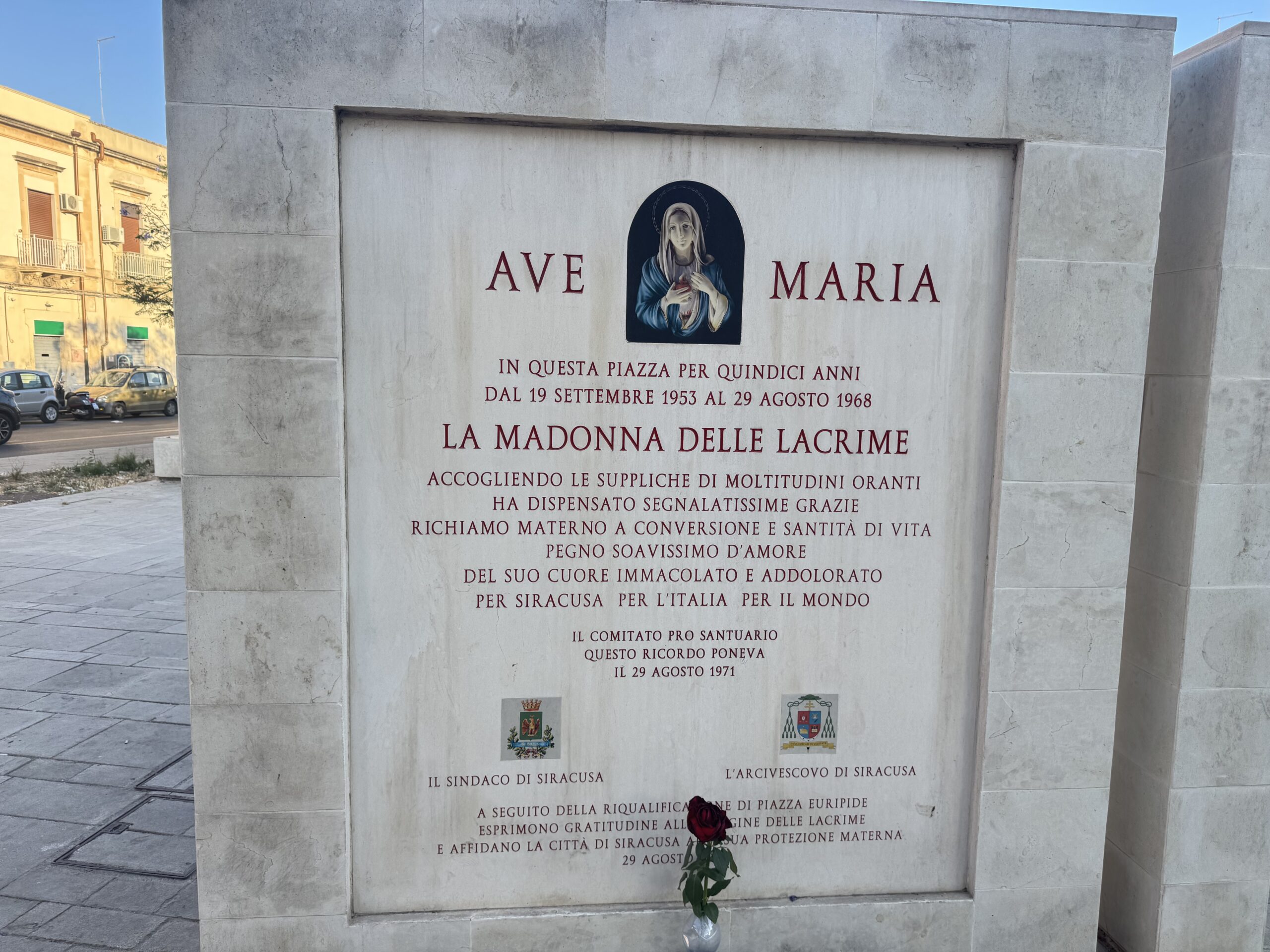 Primo piano del pannello inciso della stele: AVE MARIA con l'immagine della Madonna, il testo del 1971 del Comitato Pro Santuario e in basso gli stemmi del Sindaco e dell'Arcivescovo di Siracusa