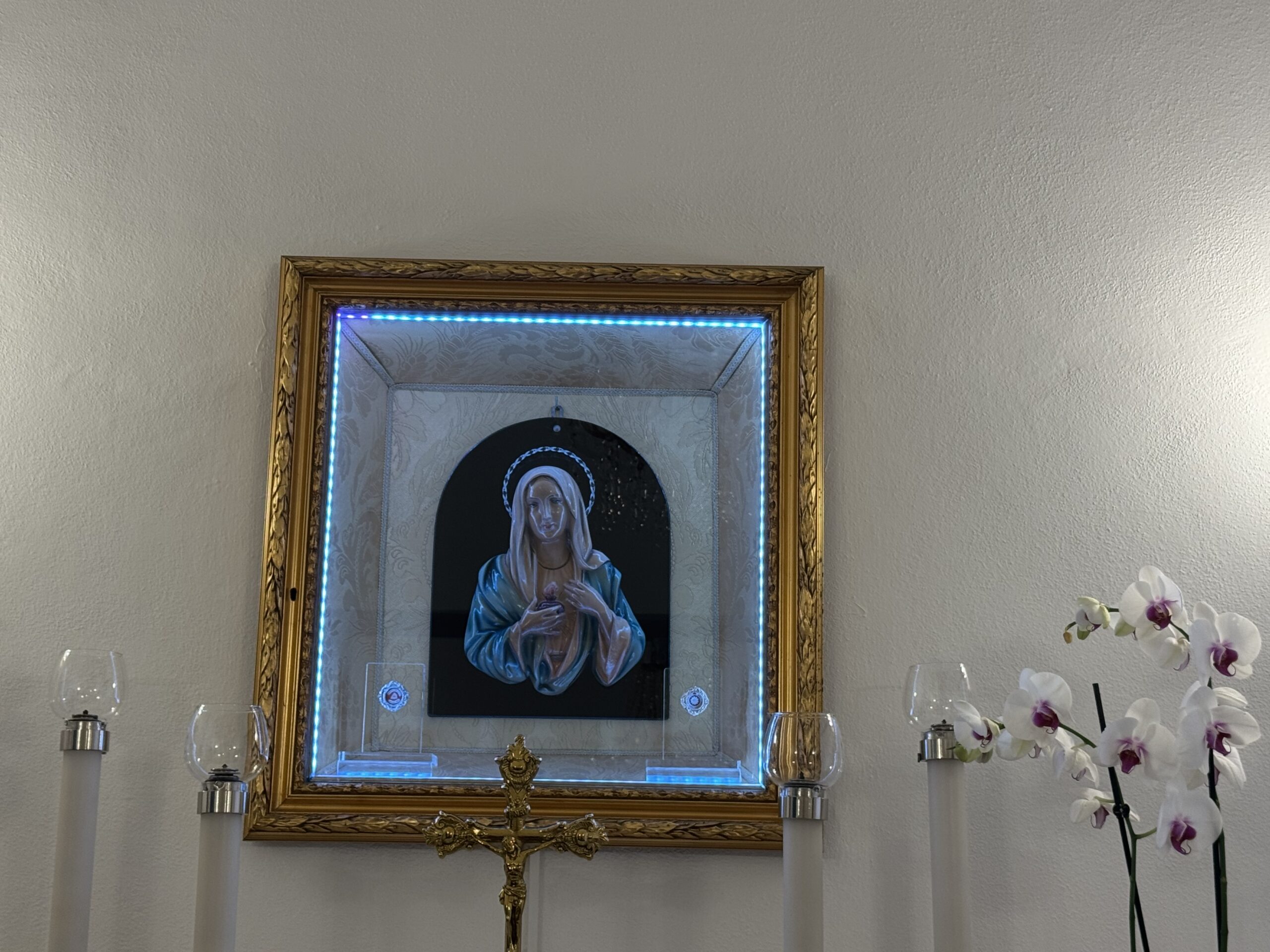 Primo piano del quadretto: bassorilievo del Cuore Immacolato di Maria con manto azzurro e mani giunte sul petto, in cornice dorata con bordo di luce azzurra, su fondo damascato