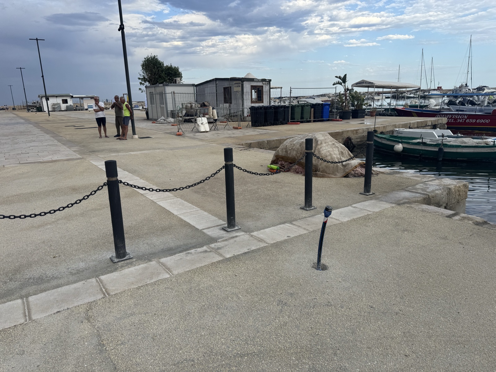 Catene tese fra paletti bassi che delimitano il piazzale dello Sbarcadero, con barche ormeggiate sul Porto Piccolo sullo sfondo.