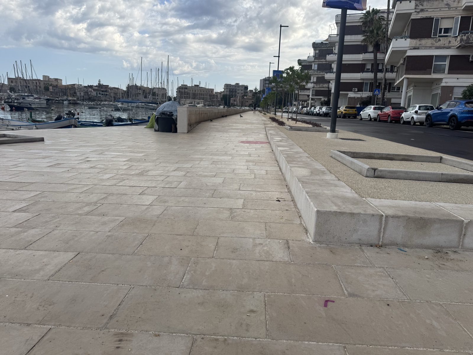 Il muretto basso in pietra lungo il margine del Porto Piccolo, con il porticciolo sullo sfondo.