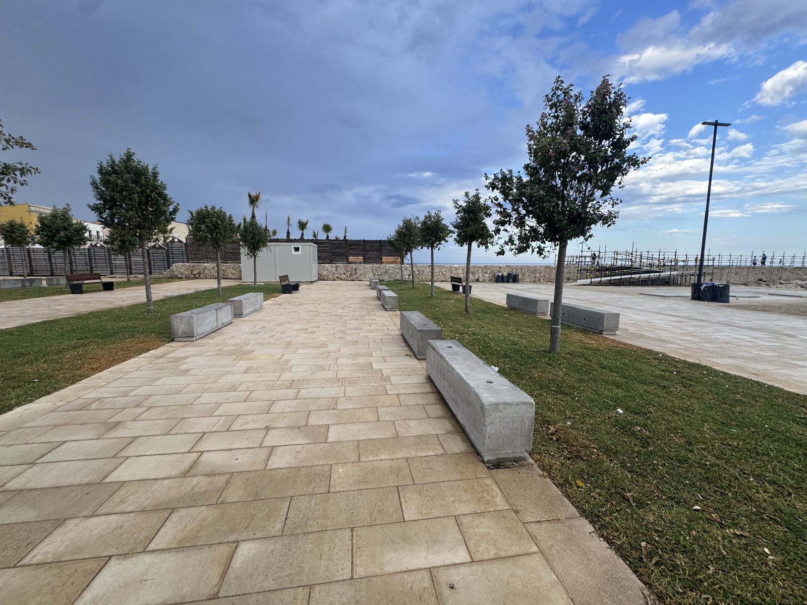 La passeggiata in pietra chiara del nuovo Sbarcadero Santa Lucia, con sedute e giovani alberi, affacciata sul Porto Piccolo di Siracusa.