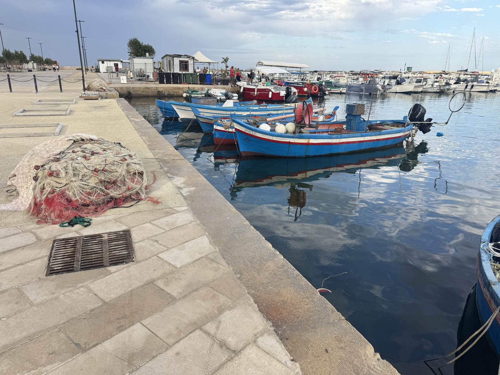 Barche da pesca ormeggiate lungo la banchina del Porto Piccolo, con reti e attrezzature nautiche sulla riva.
