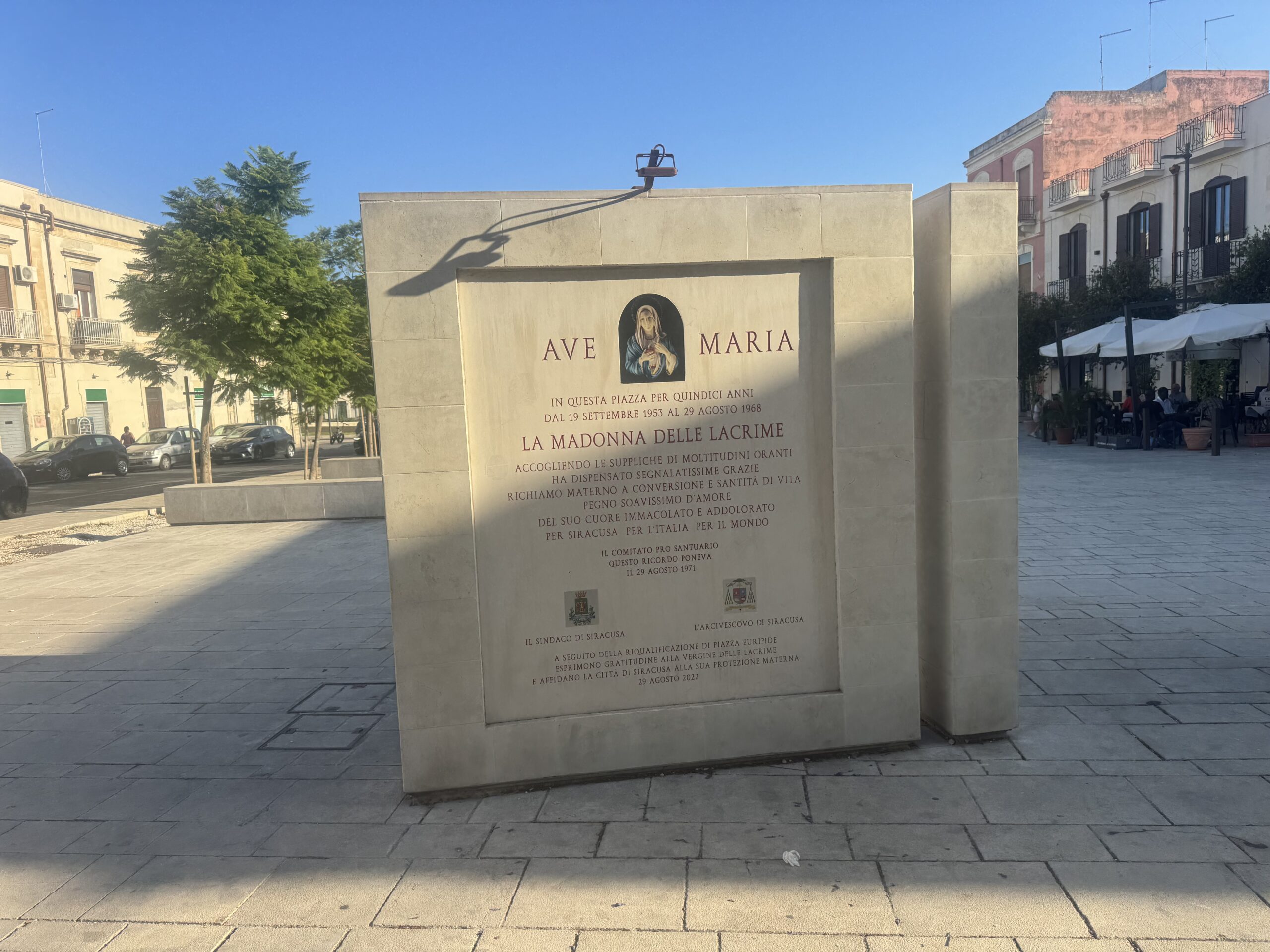 Fronte della stele con l'immagine ceramica del Cuore Immacolato di Maria, la scritta AVE MARIA e una lunga iscrizione incisa, nella piazza pavimentata