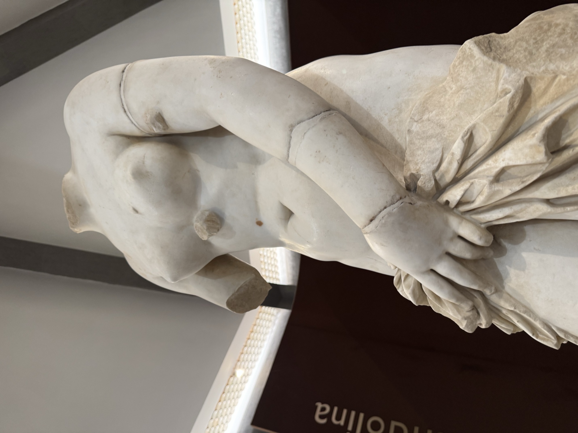 Dettaglio del torso e della mano che trattiene il lembo del panneggio davanti al corpo