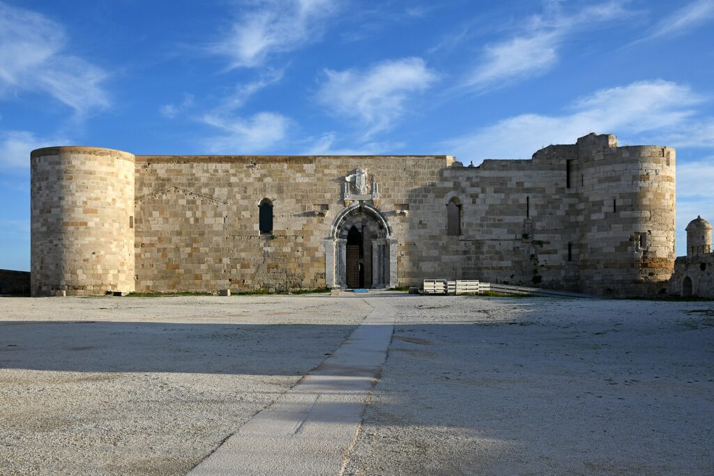 Il Castello Maniace visto dal mare: la mole quadrata in pietra calcarea sulla punta di Ortigia, con le torri cilindriche angolari
