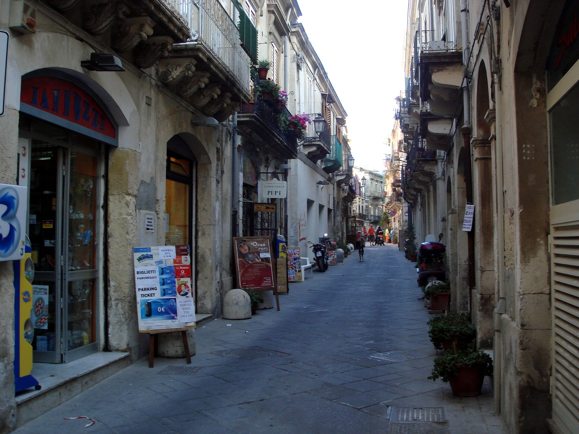 La stretta via della Giudecca a Ortigia con palazzi in pietra bianca, balconi in ferro battuto e l'insegna del laboratorio dei pupi