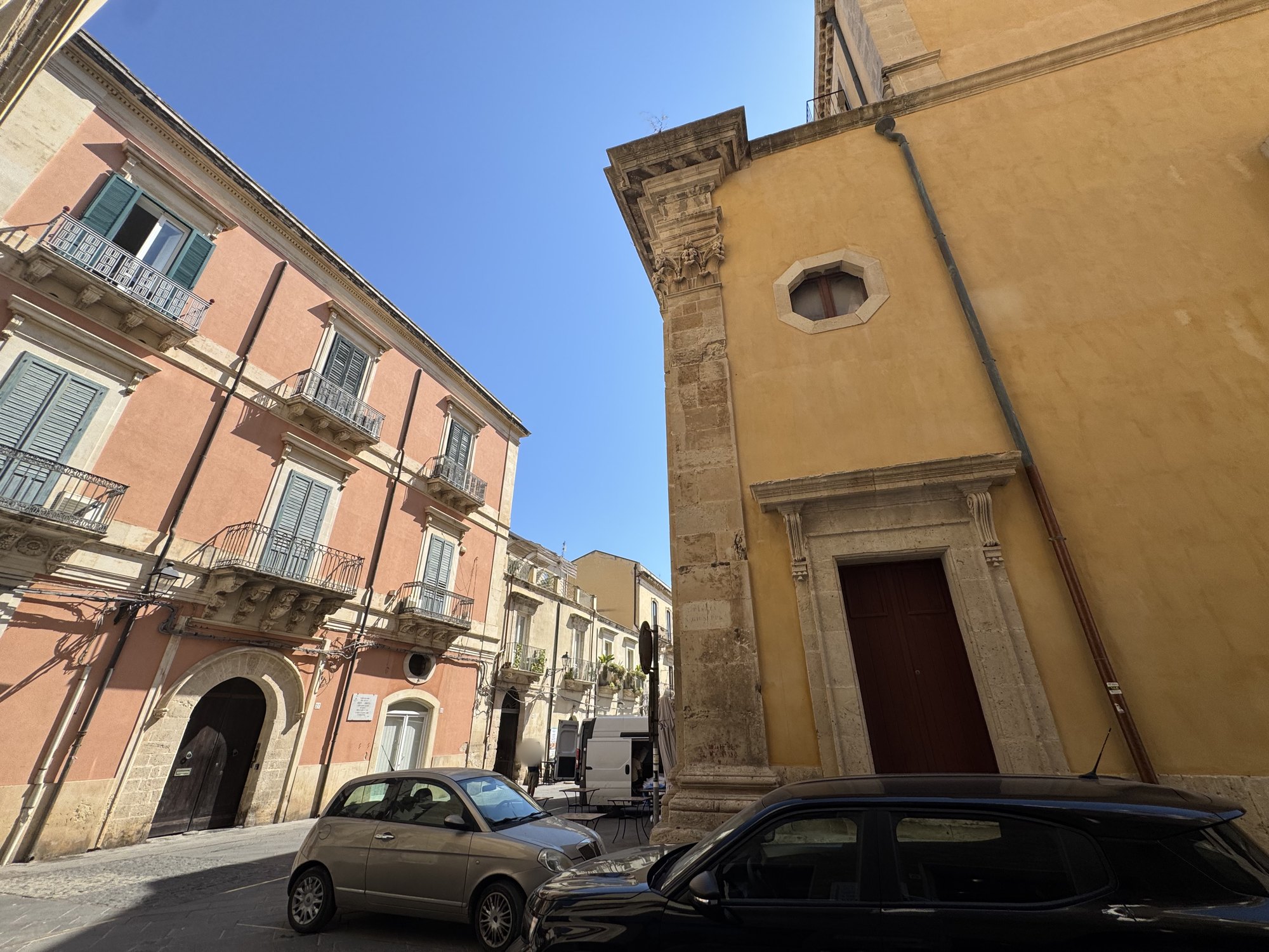 Scorcio fra la chiesa e un palazzo storico rosa con balconi in ferro battuto e una lapide marmorea