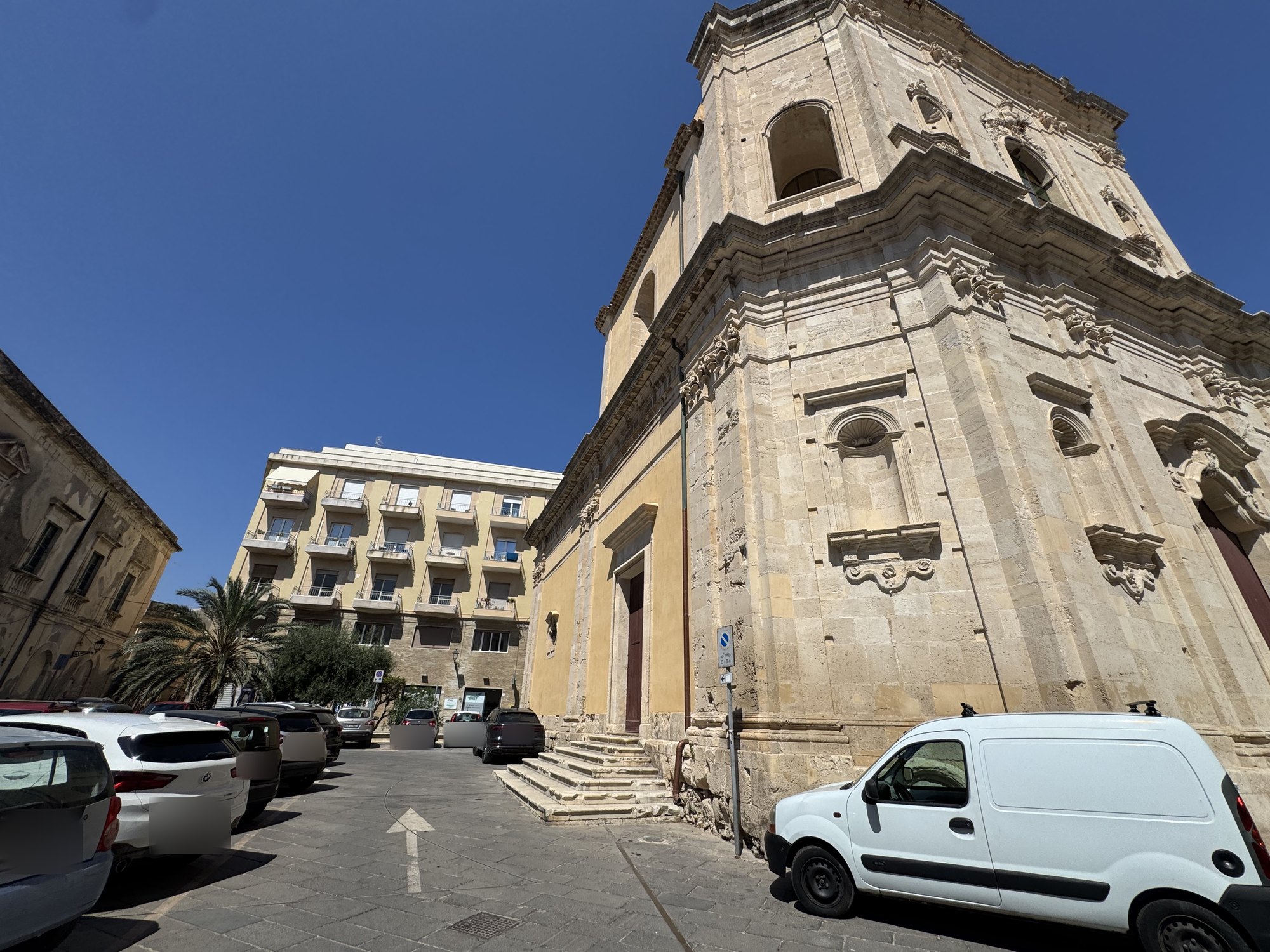 Fianco della chiesa intonacato di ocra con portale laterale e gradini, sullo sfondo un condominio moderno