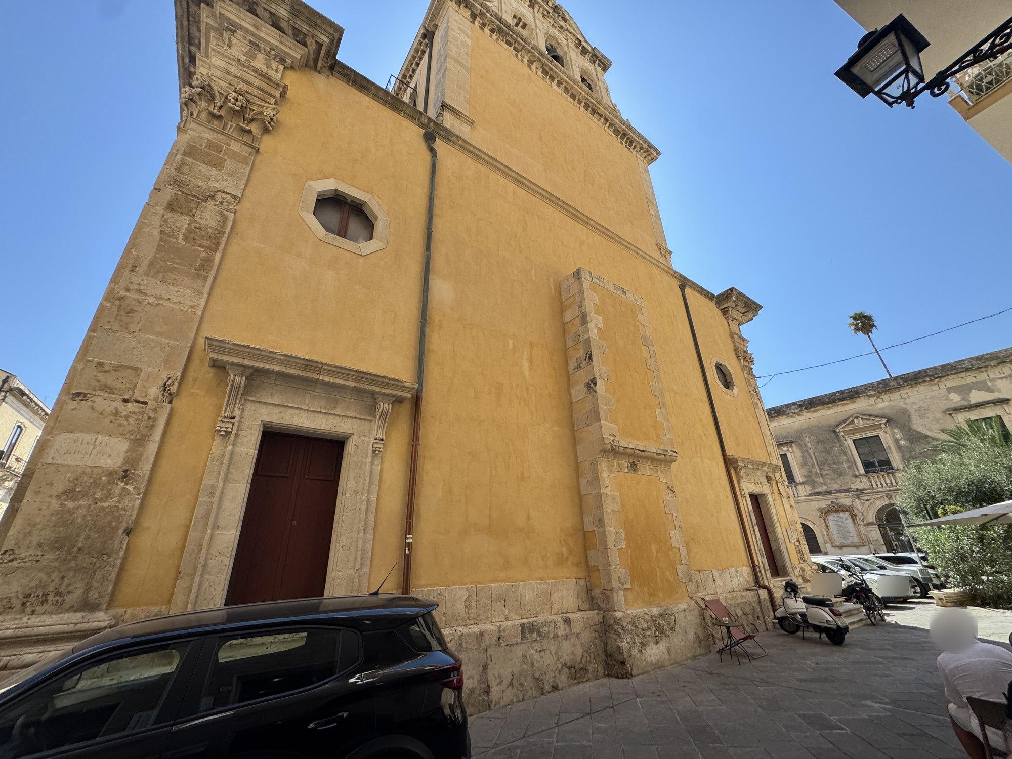 Lunga parete laterale intonacata di ocra su alto basamento in pietra, con un grande riquadro rettangolare in conci di pietra murato e una finestra ottagonale in alto