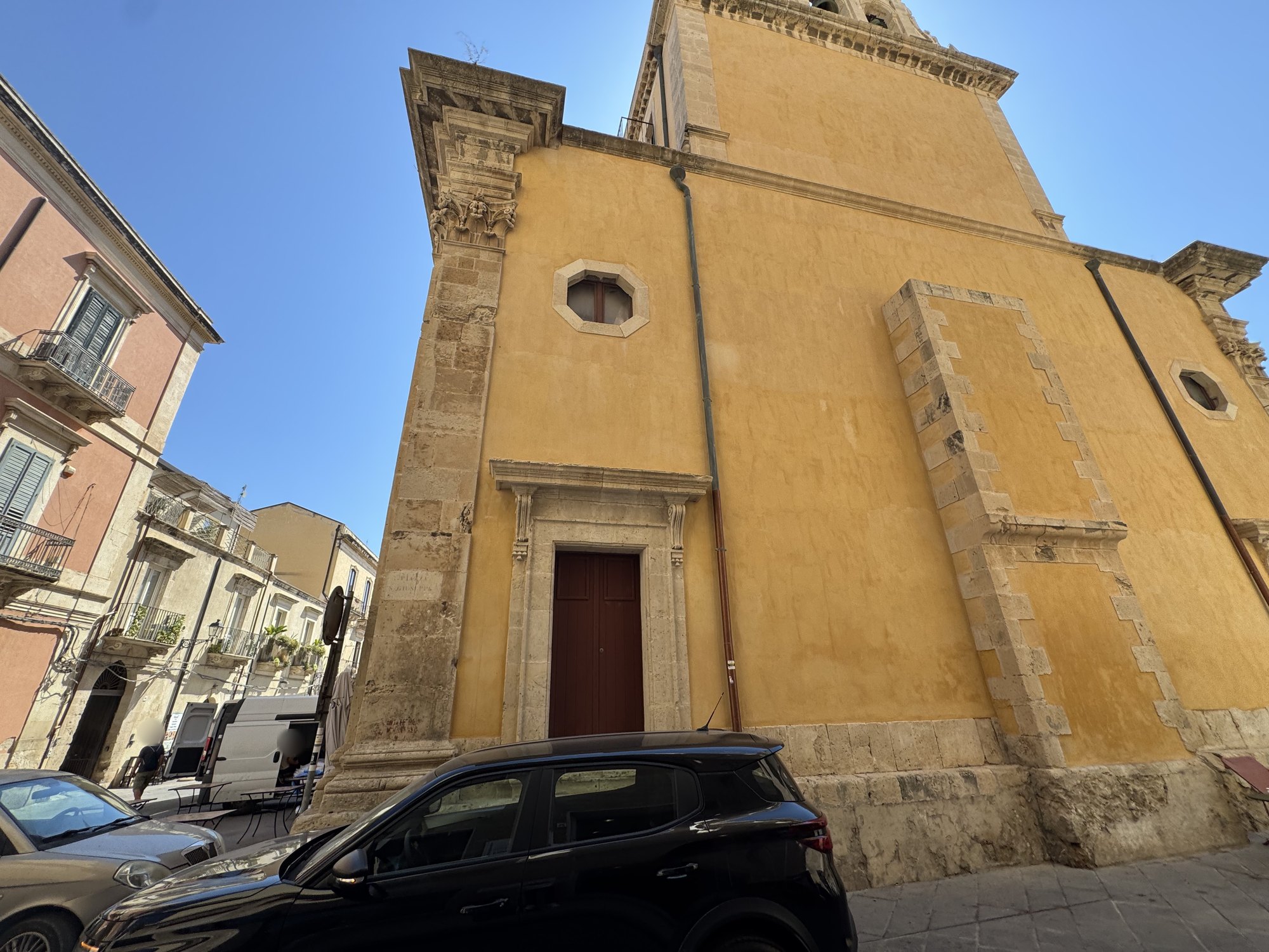 Parete laterale con portale incorniciato in pietra, finestra ottagonale in alto e cantonale in conci con una vecchia scritta dipinta