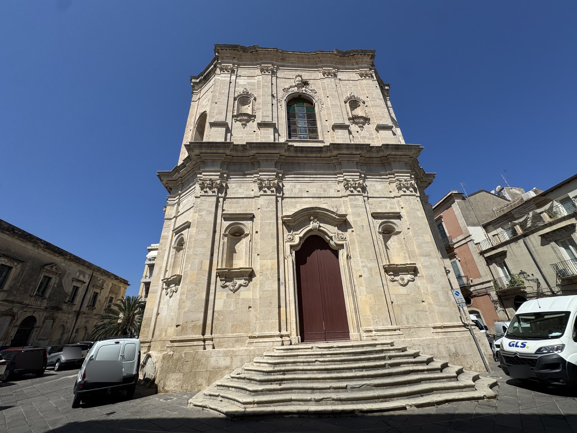 Portale barocco con cornice scolpita, arco mistilineo e cartiglio con stemma coronato al centro, affiancato da due nicchie vuote con catino a conchiglia su mensole a voluta