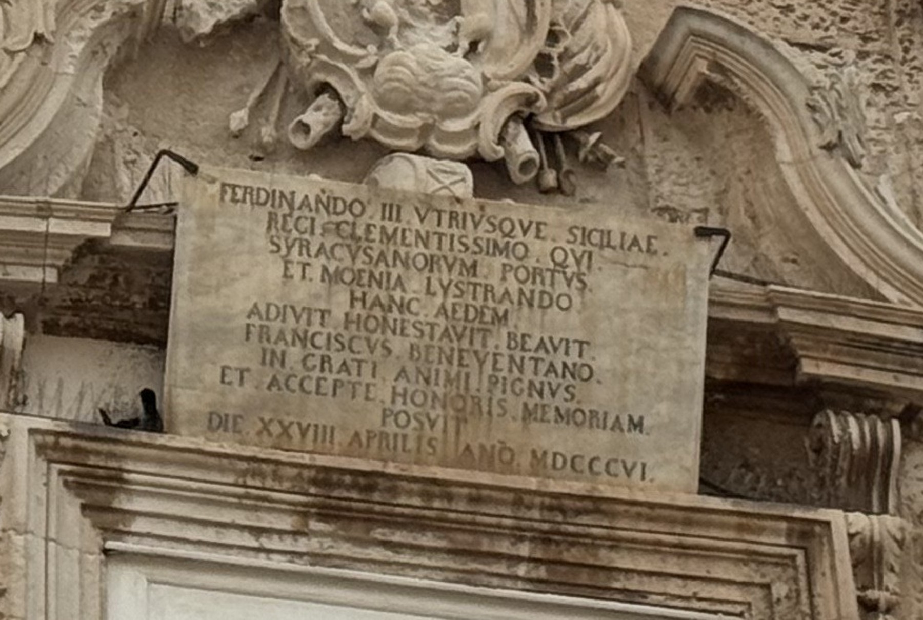 Dettaglio ravvicinato della lapide in pietra con undici righe di iscrizione latina a lettere capitali, sormontata da un cartiglio scolpito