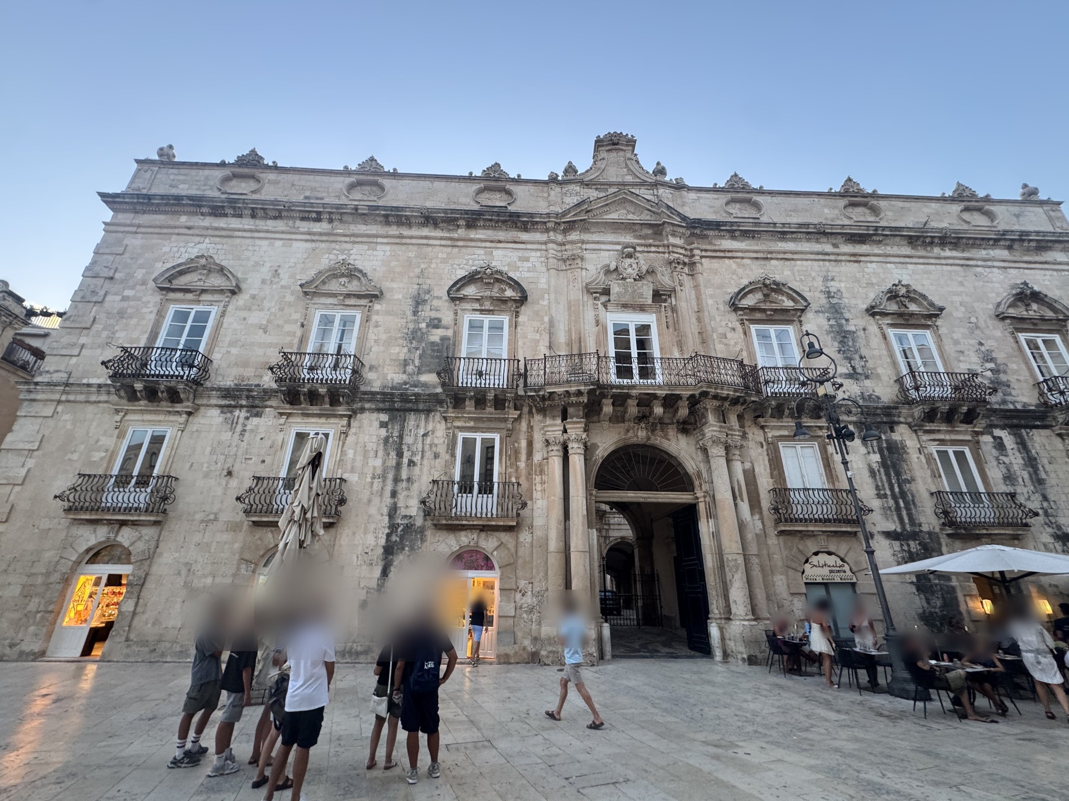 Il portale ad arco con i battenti scuri aperti, affiancato da colonne su alti plinti, e la pavimentazione chiara della piazza in primo piano