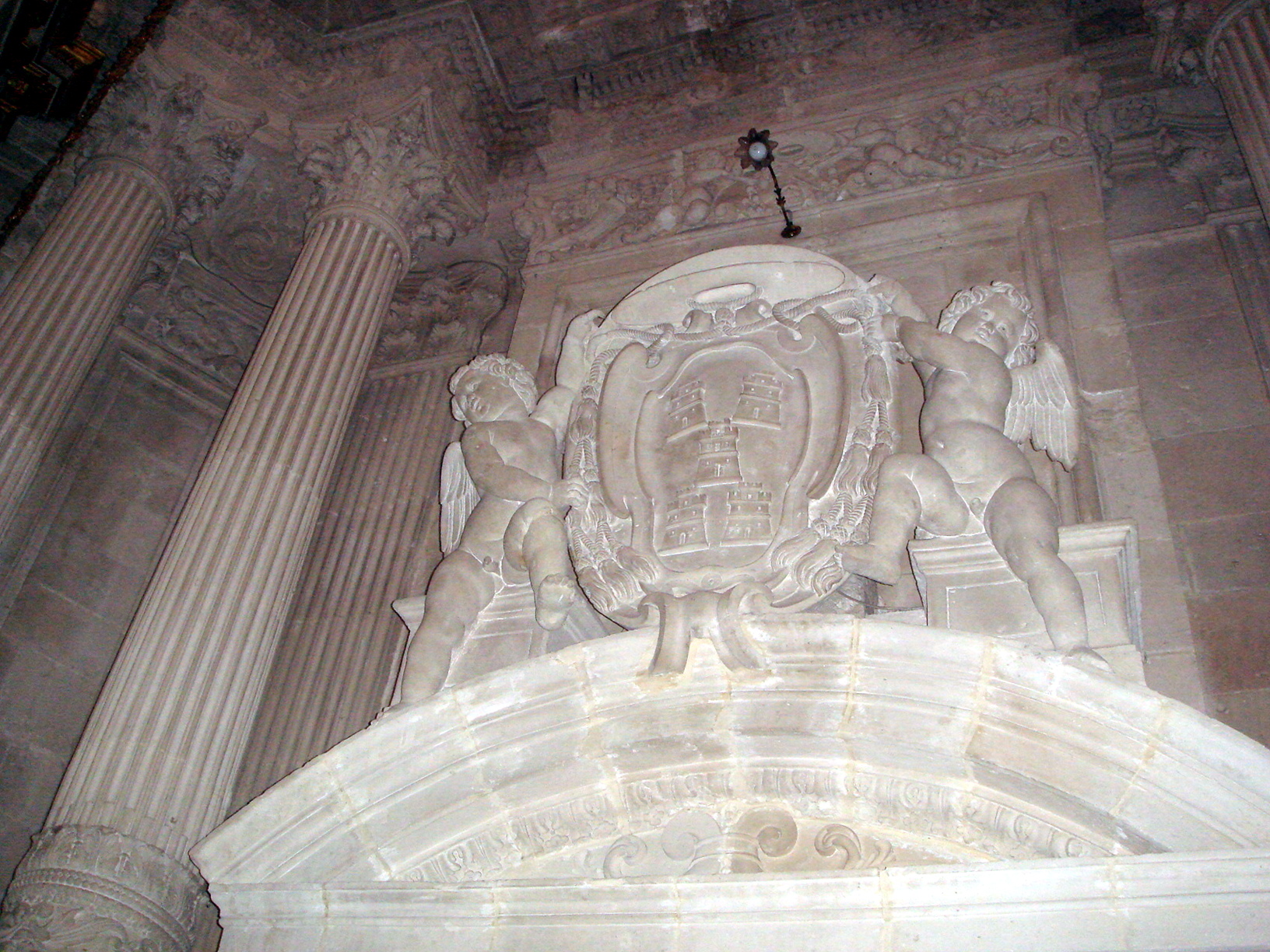 Stemma lapideo con cinque torri disposte in decusse, retto da putti alati e sormontato dal galero, sul portale della cappella del Sacramento