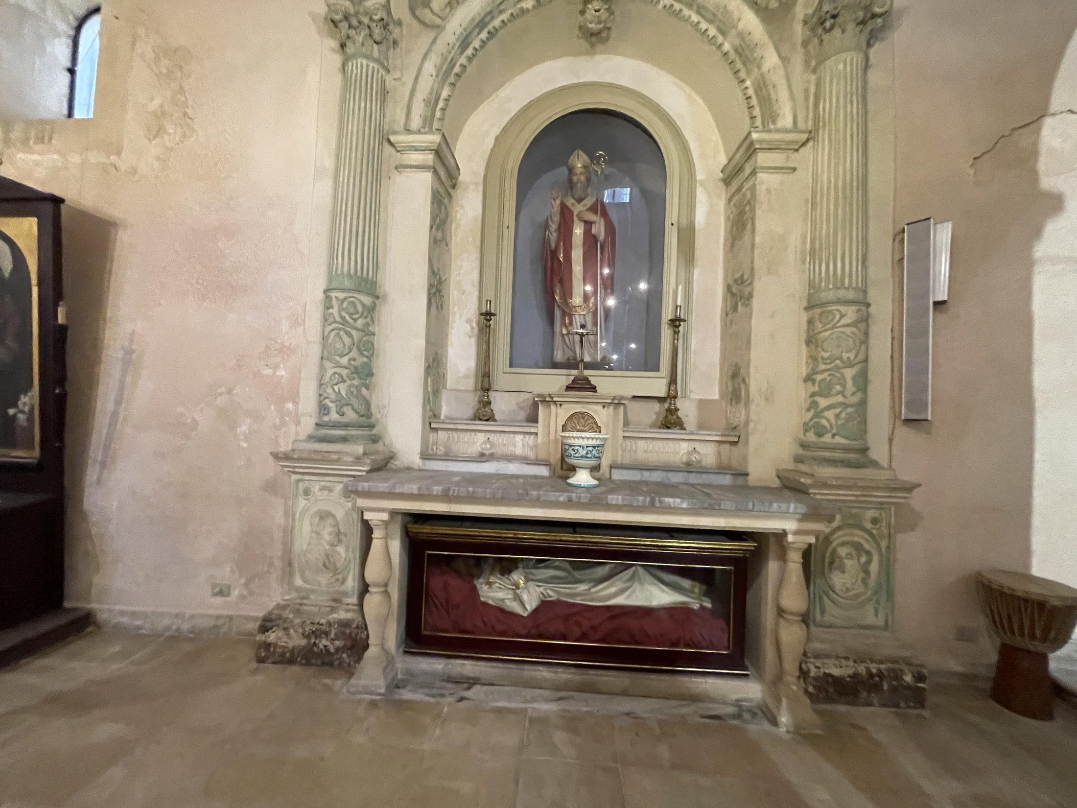 Altare barocco in pietra e stucco con colonne decorate e nicchia con la statua di un santo vescovo; sotto la mensa l'urna di vetro con il corpo del martire