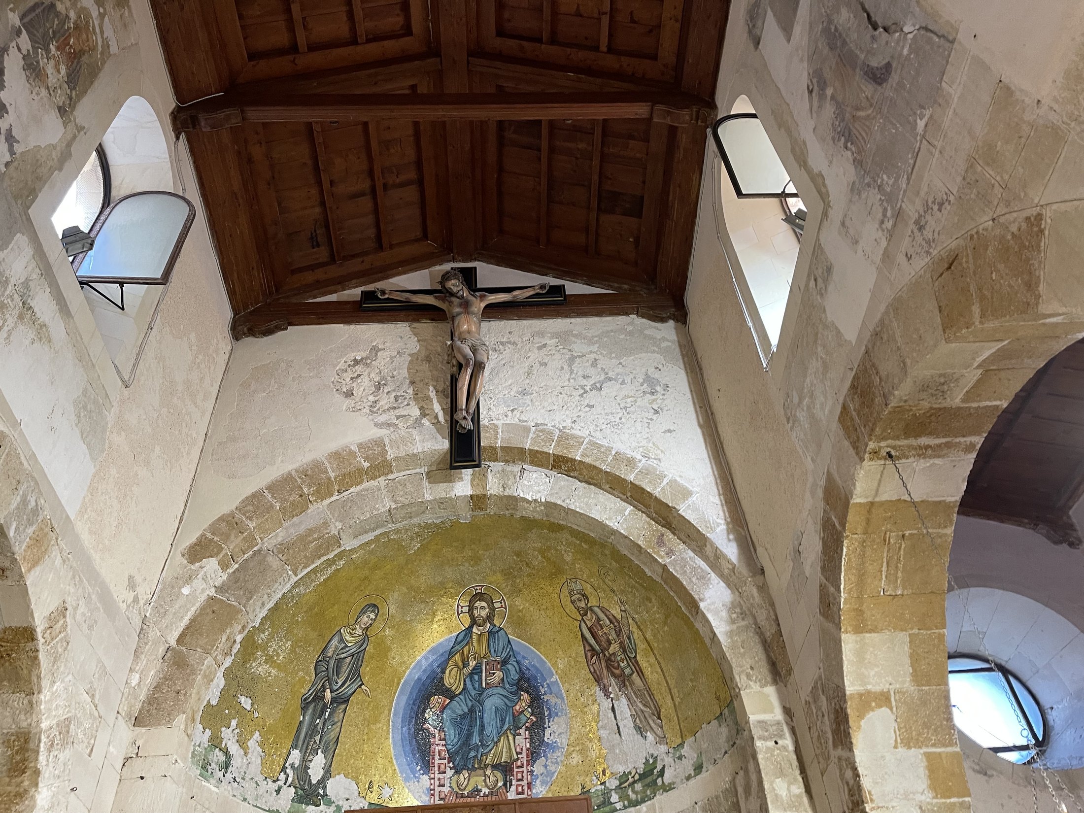 L'arco absidale a doppia ghiera, il soffitto a capriate lignee con mensole, le finestre centinate del cleristorio e il catino absidale dipinto a fondo oro con Cristo in trono fra due santi