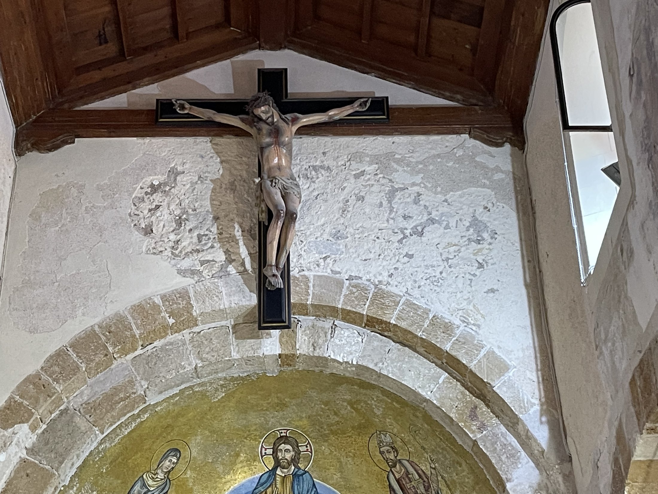 L'arco absidale a doppia ghiera di conci con il crocifisso ligneo sospeso e, sotto, il catino absidale a fondo oro con Cristo in trono