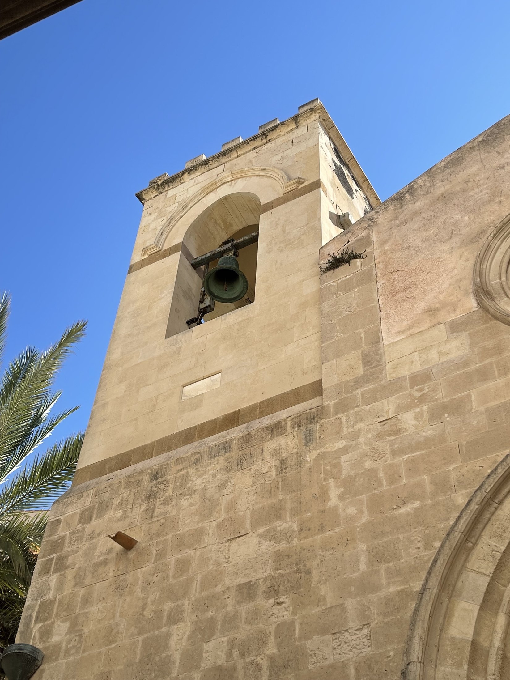 Il campanile a torre in conci chiari con la cella campanaria ad arco a tutto sesto, la campana appesa a una trave e il coronamento a merli