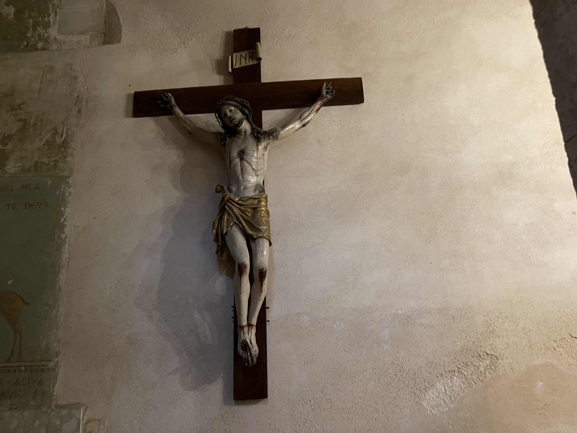 Crocifisso ligneo con Cristo policromo e perizoma dorato, appeso a una parete di pietra