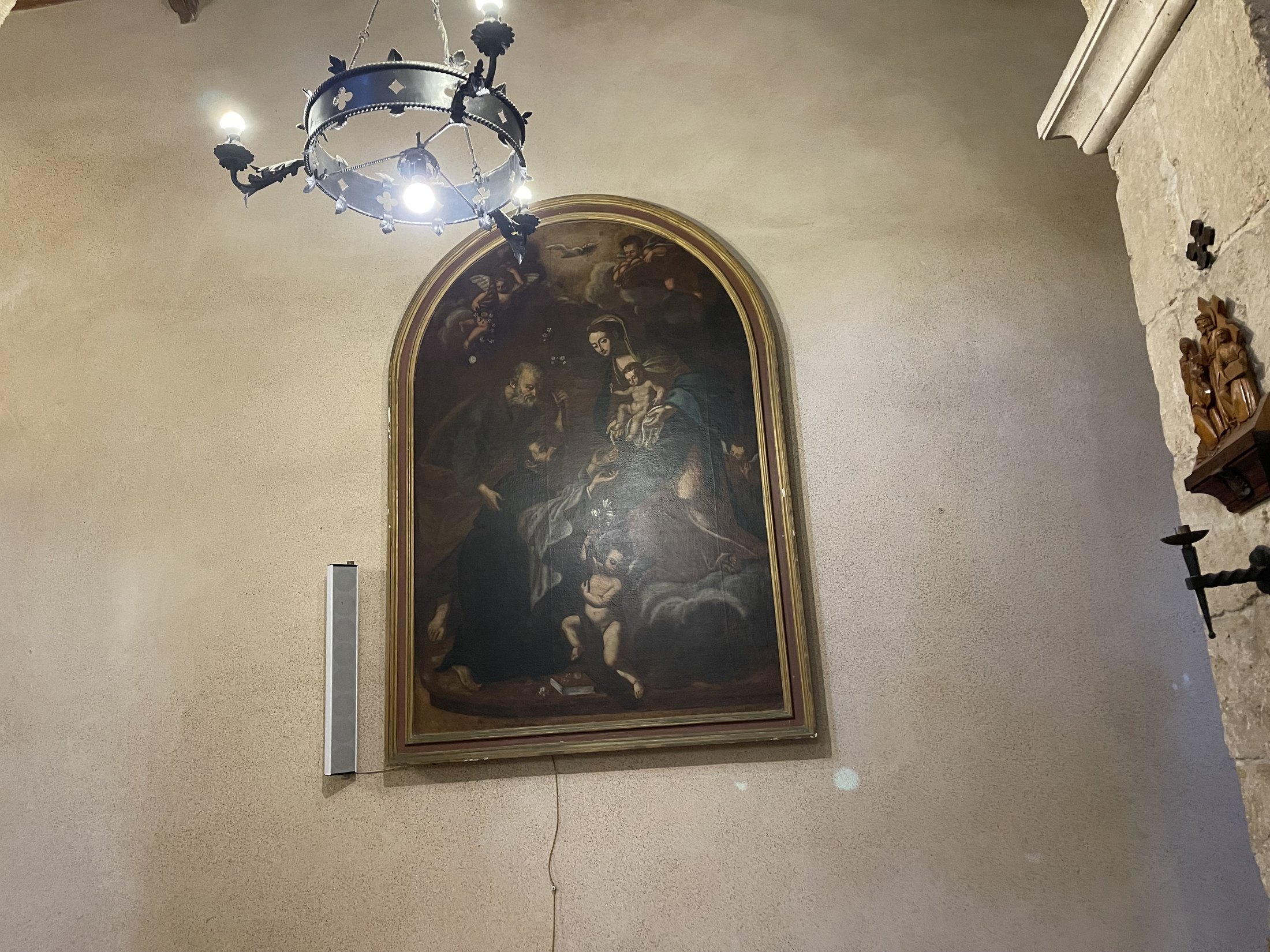 Grande dipinto centinato con cornice dorata appeso alla parete di una navatella, illuminato da un lampadario circolare