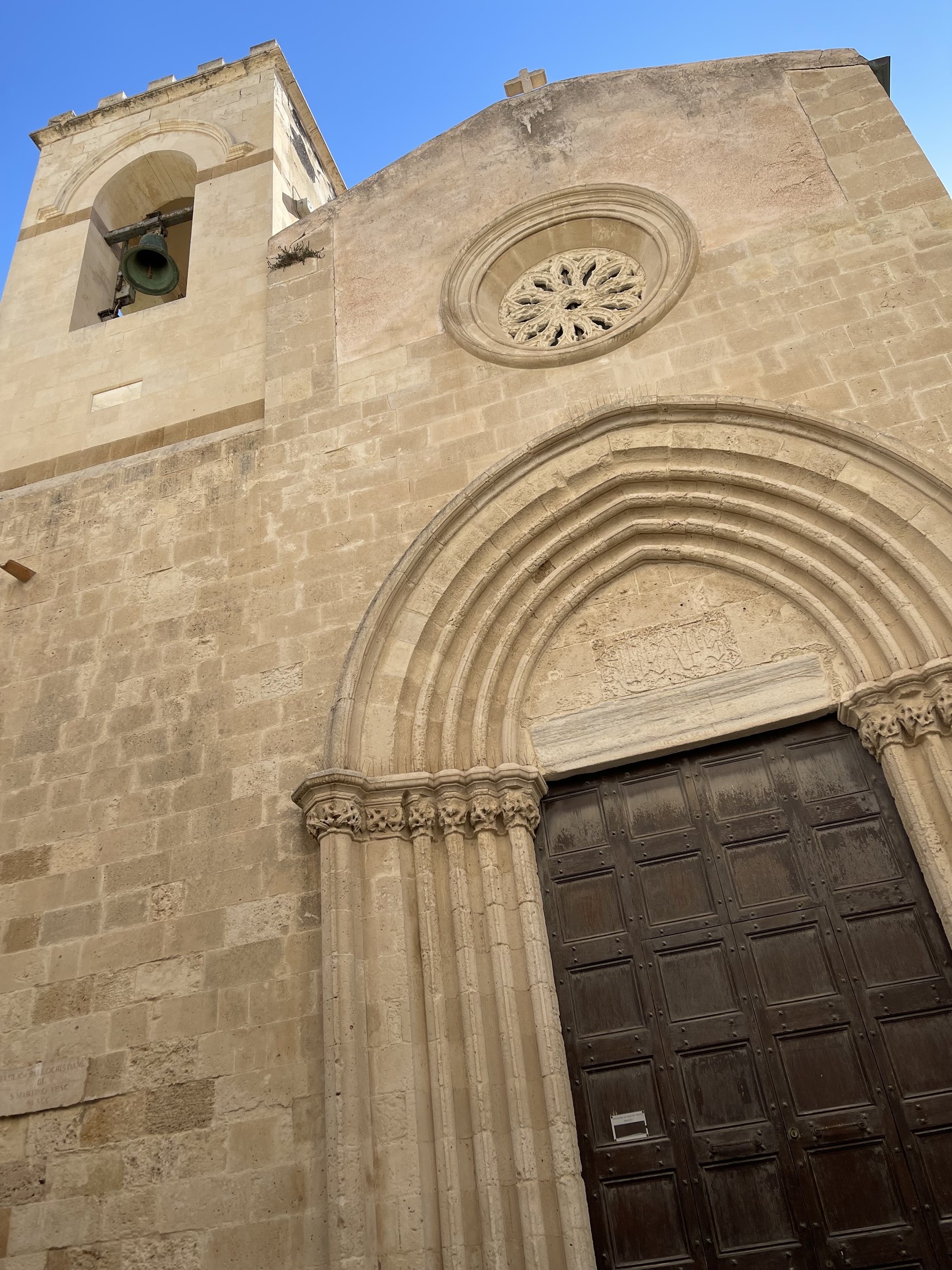 La facciata vista dal basso: il portale a sesto acuto con quattro ghiere e i fasci di colonnine, il rosone traforato, il campanile con la campana nella cella ad arco