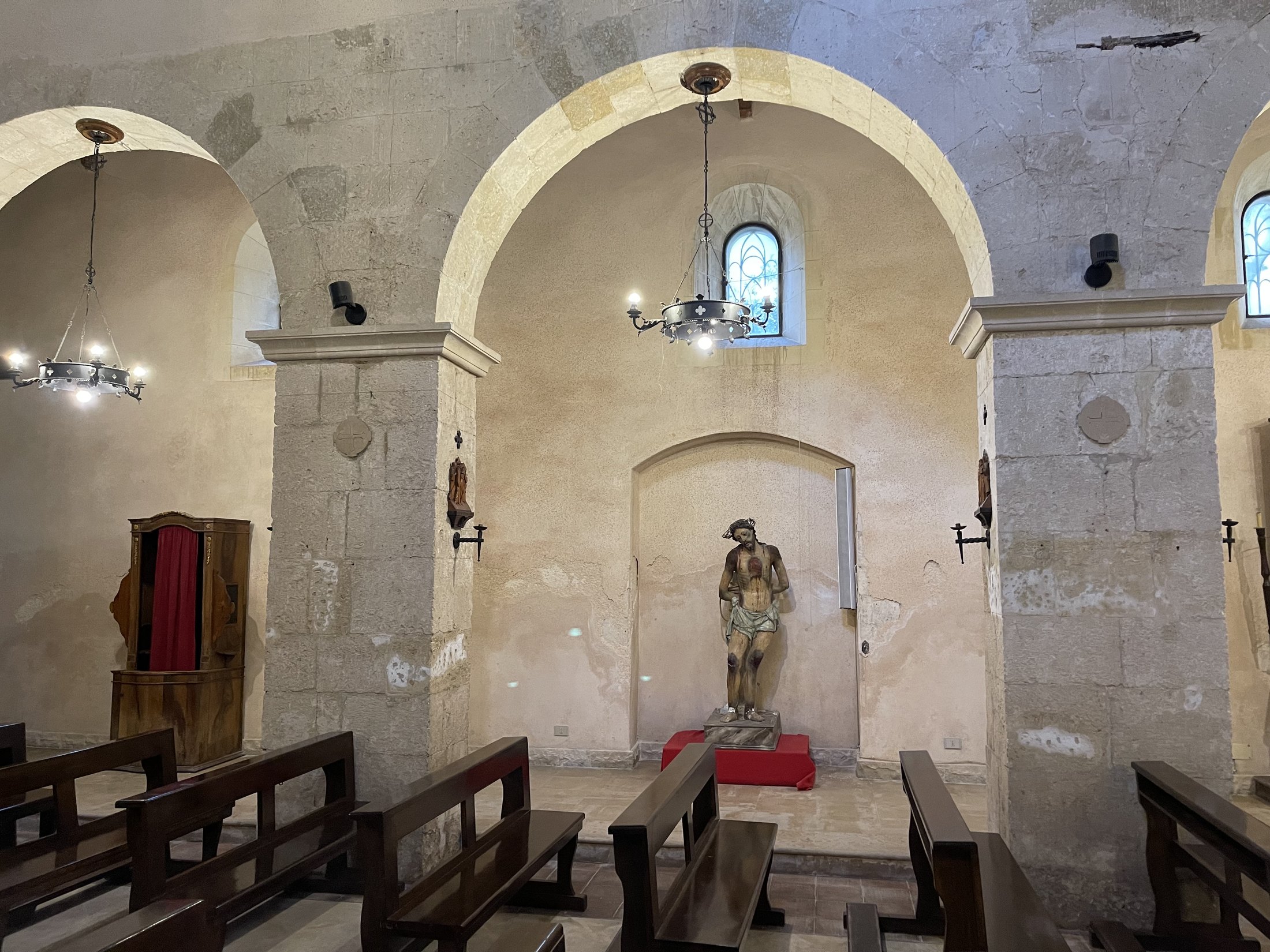 Fondo di una navatella con archi in conci, la statua dell'Ecce Homo su base rossa, un confessionale e una finestra centinata