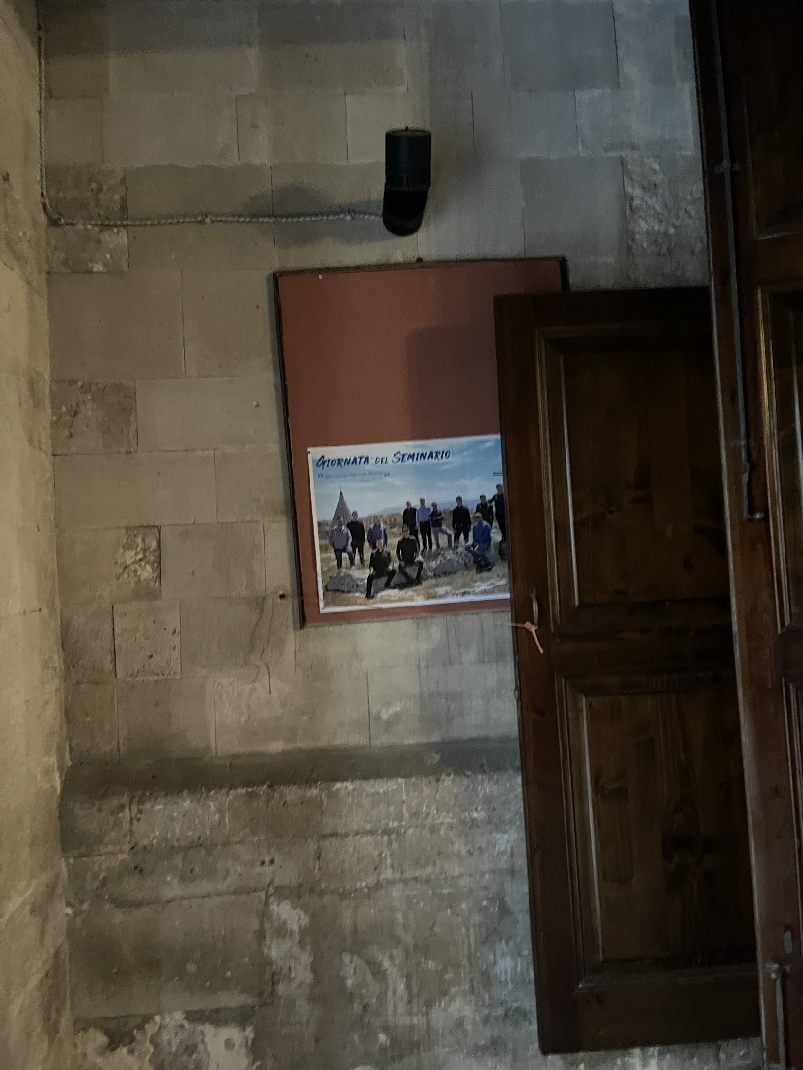 Porta di legno a due battenti nel muro meridionale, con una bacheca accanto e le pareti in conci