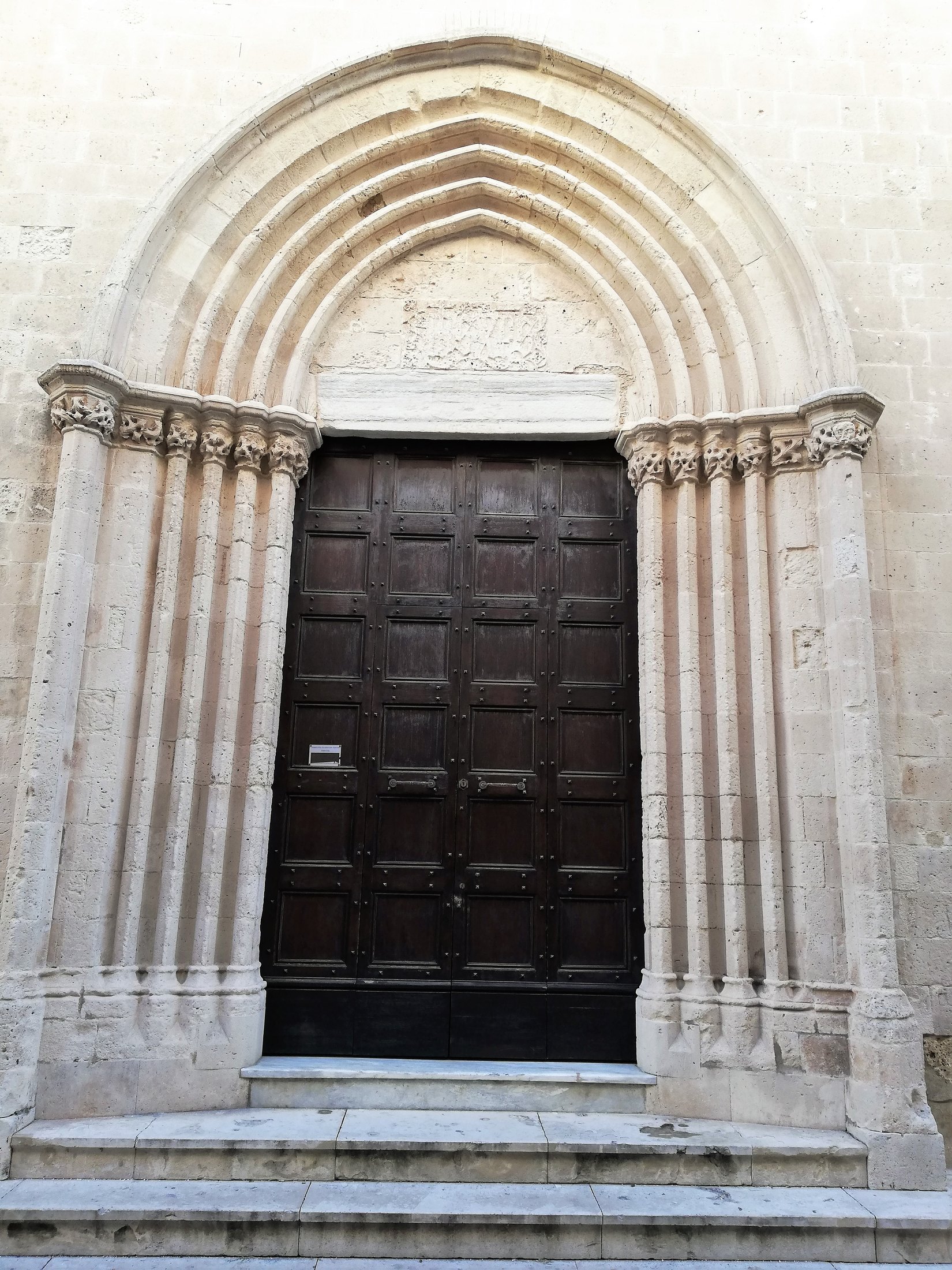 Il portale a sesto acuto visto di fronte: quattro ghiere a toro digradanti e, per lato, un fascio di cinque colonnine a rocchi concluse da capitelli a fogliame