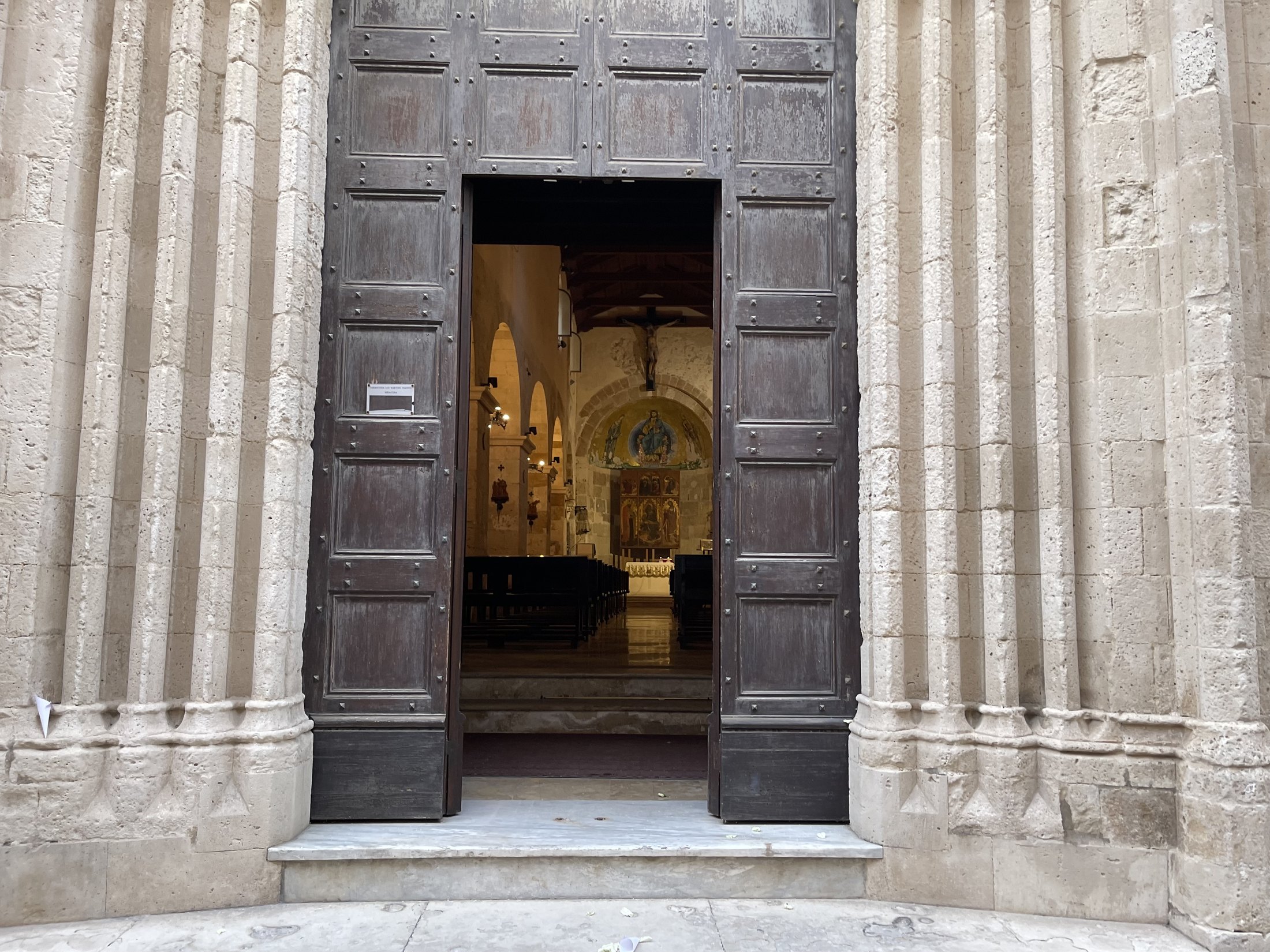 Il portale con i battenti di castagno aperti, i fasci di colonnine ai lati e, in fondo, la navata illuminata con l'abside dorata