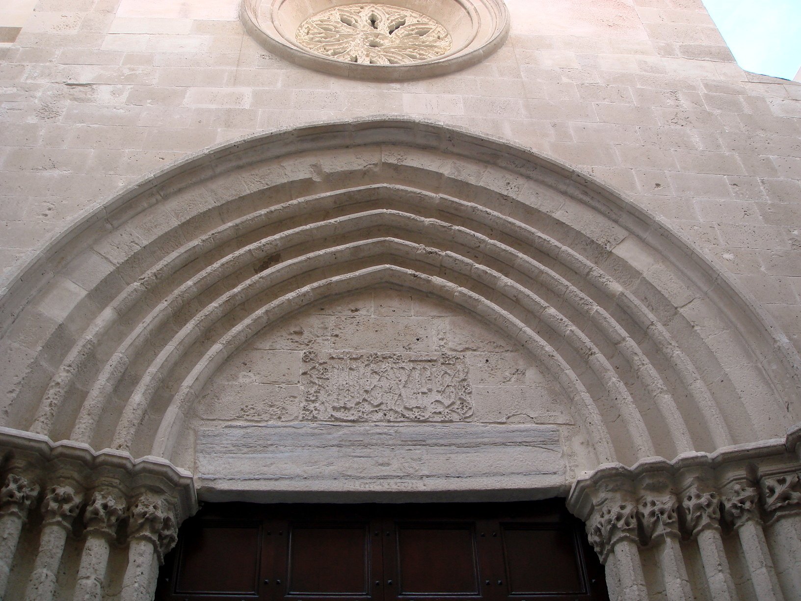 Parte alta del portale: le ghiere a toro, la lunetta tamponata a conci con il riquadro scolpito del monogramma consunto e l'architrave di marmo venato