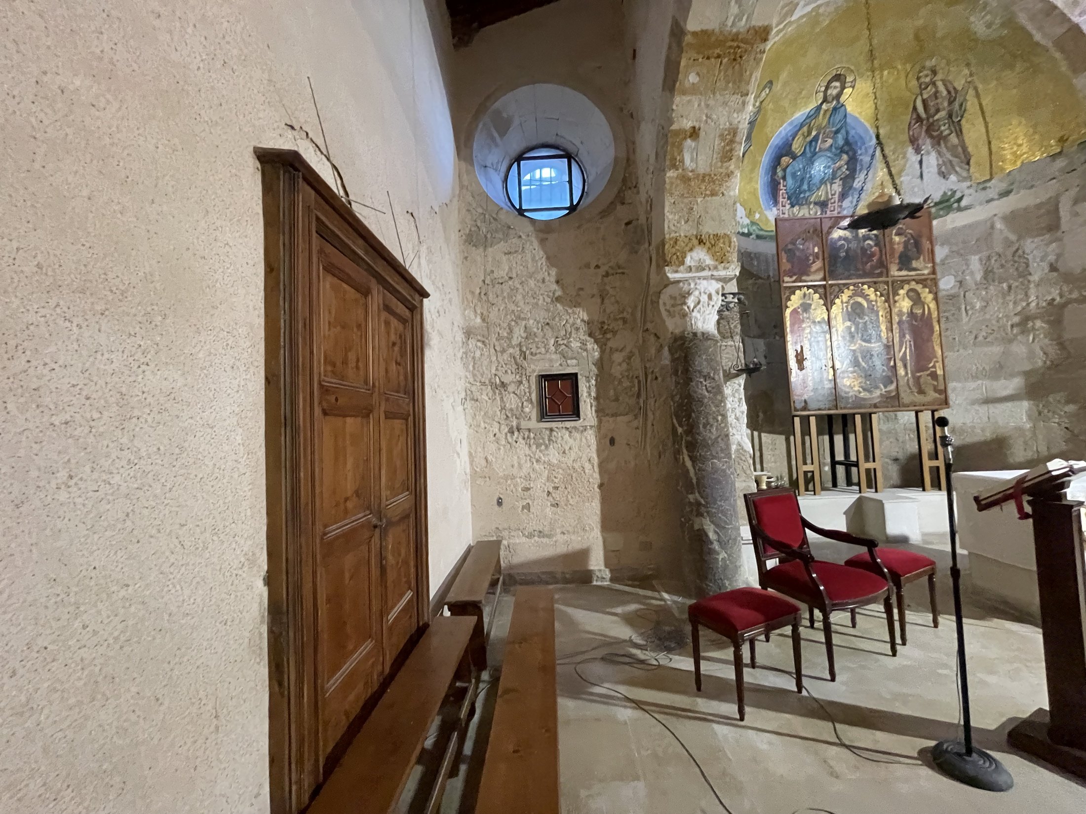 Zona presbiteriale con un polittico gotico a sei tavole su cavalletto, una colonna antica di granito grigio con capitello bianco, un armadio a muro di noce e un oculo con grata