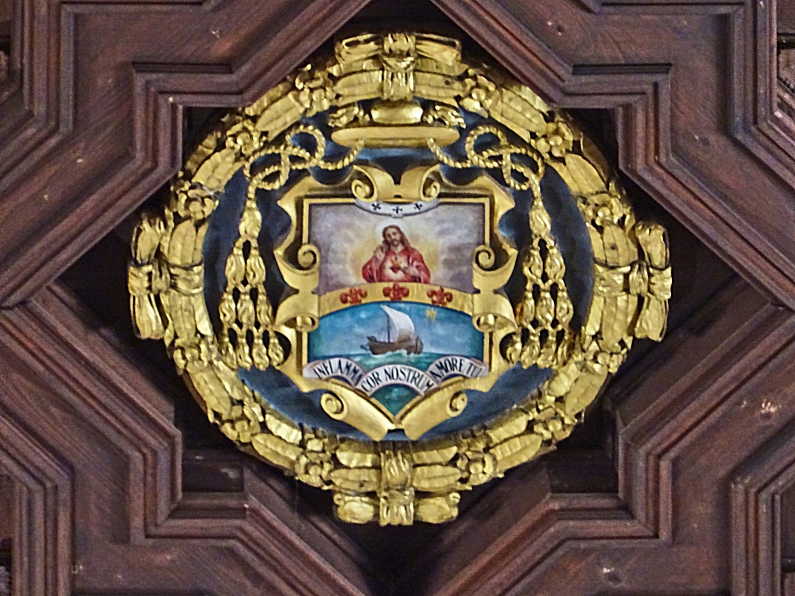 Dettaglio del soffitto ligneo del Duomo di Siracusa: una cornice a stella racchiude uno stemma ecclesiastico dipinto, ornato da mitra, cappello con nappe e decorazioni dorate. Lo scudo raffigura il Sacro Cuore nella parte alta e una barca a vela sul mare sotto una stella in quella bassa; un cartiglio reca un motto latino.
